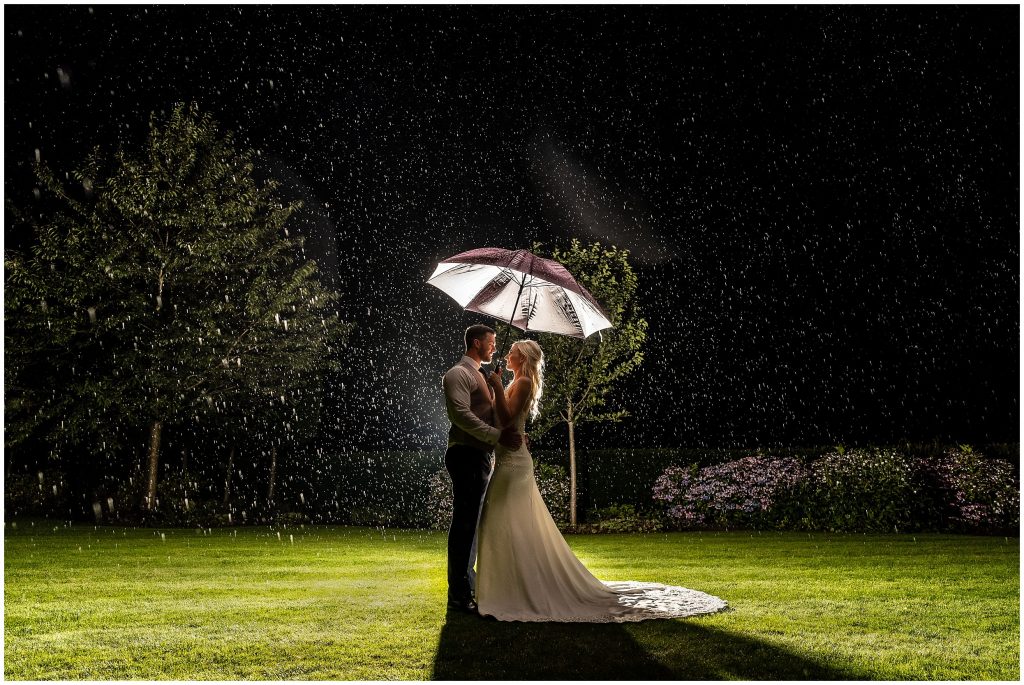 Bride and groom under an umbrella in the rain at night