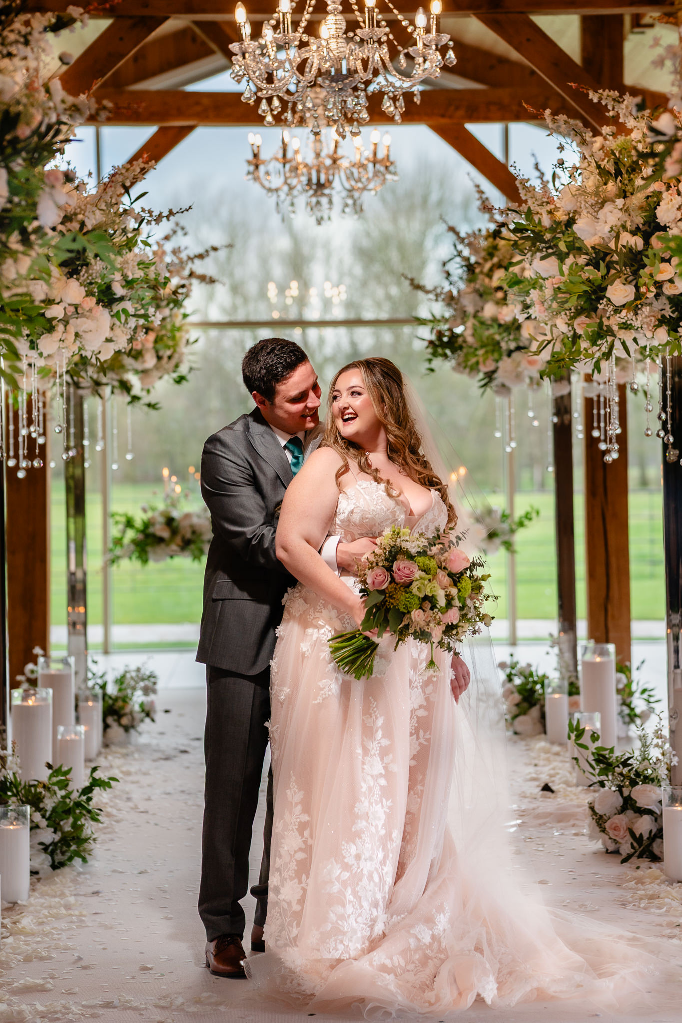Bride and groom embracing under the floral arch at Merrydale Manor’s glass ceremony room