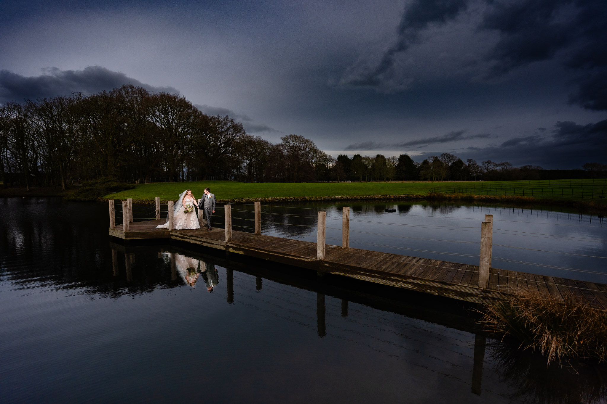 Bride and groom walking hand in hand along the lake jetty at dusk, Merrydale Manor wedding photographer