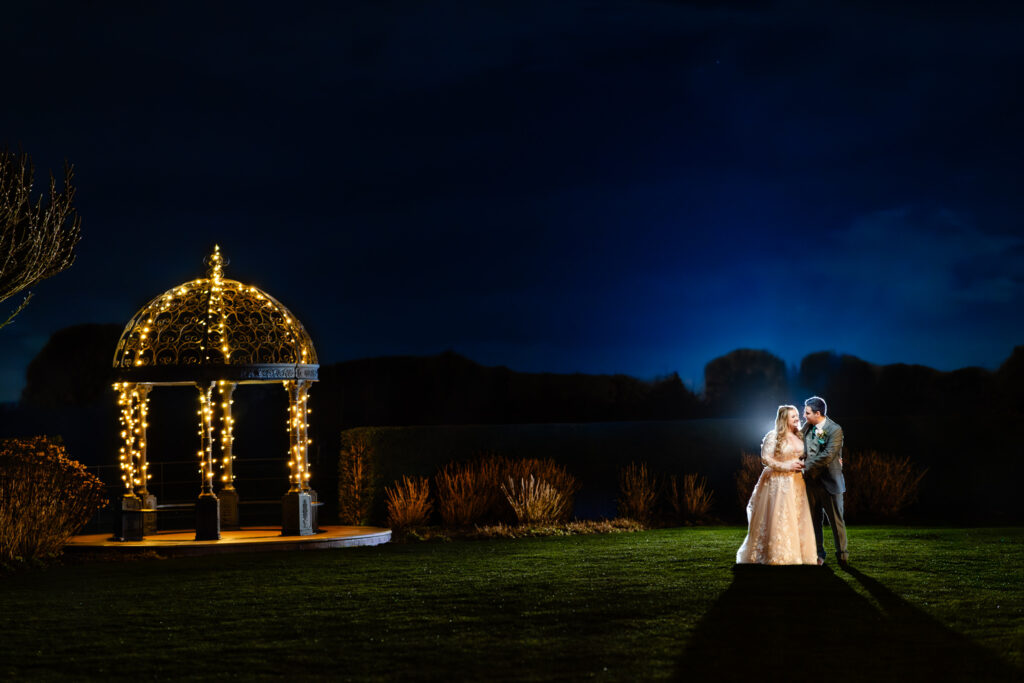 Bride and groom by the fairy light gazebo in the gardens at Merrydale Manor at night