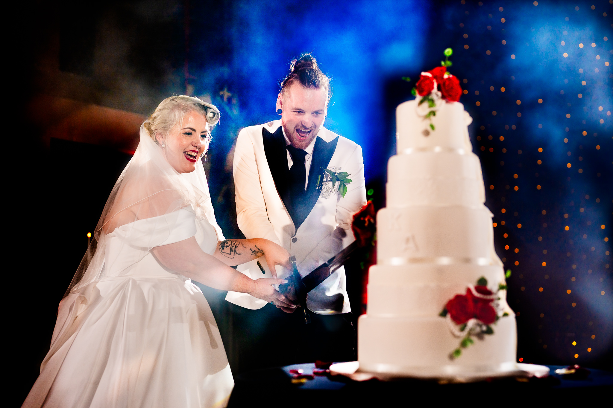 Bride and groom cutting their wedding cake, lit with blue and red off camera flash