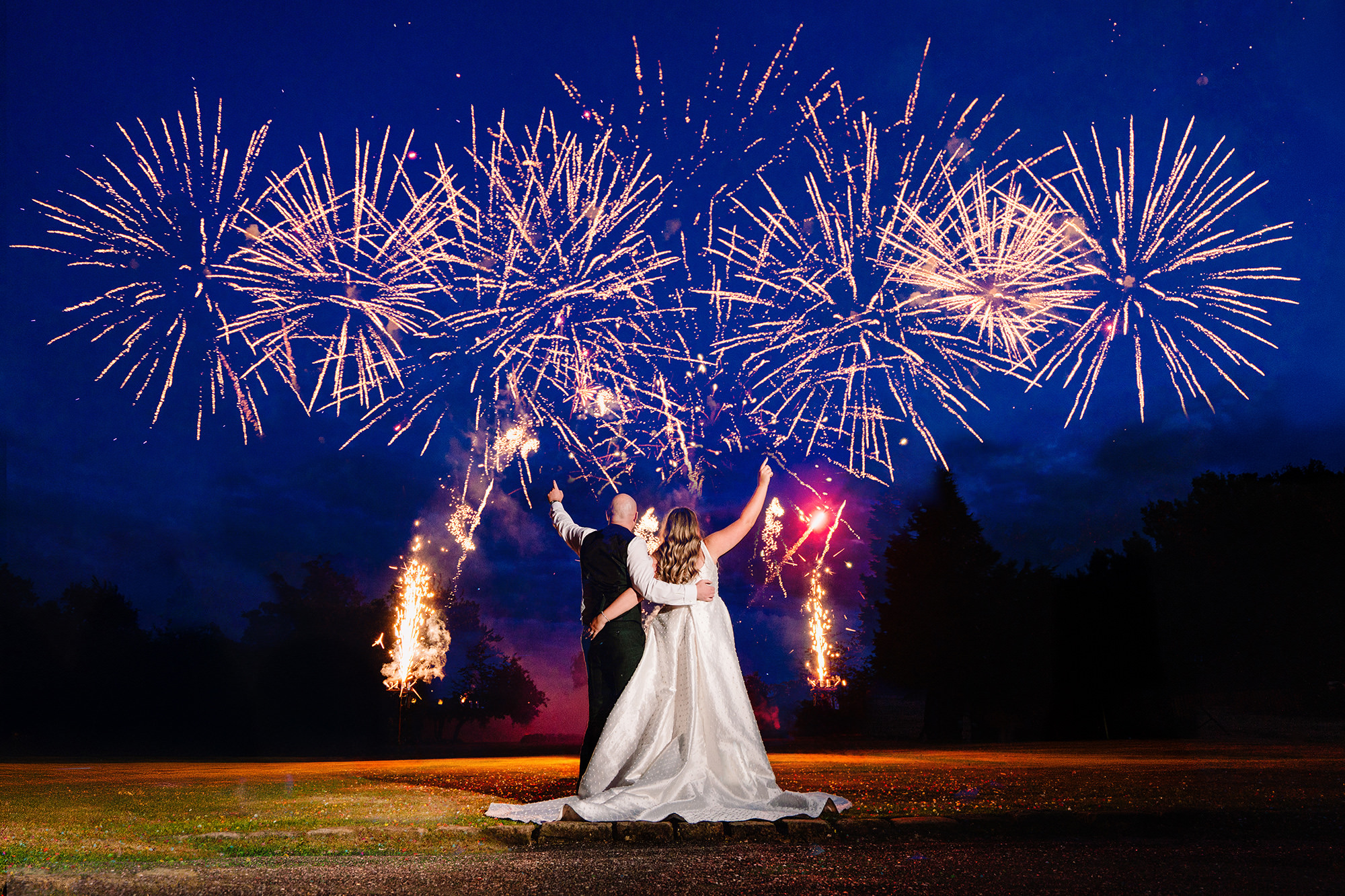 Bride and groom photographed at night in front of fireworks, lit with off camera flash