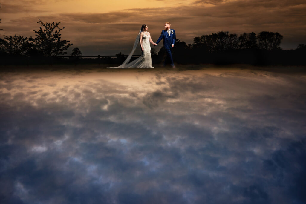 Bride and groom photographed at dusk under a dramatic sky, lit with off camera flash