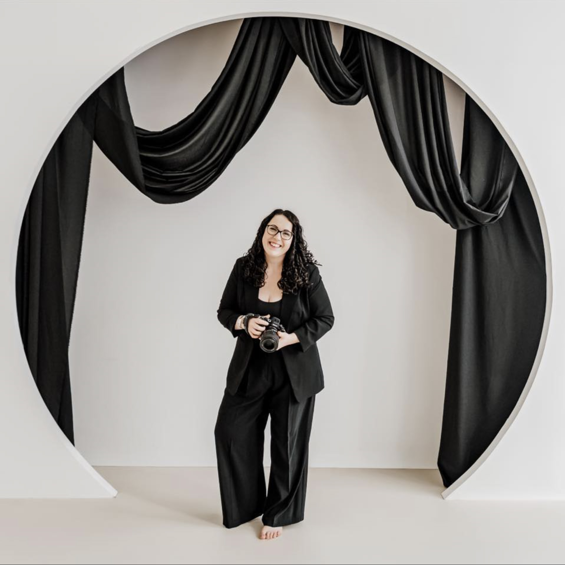 Megan Maxwell, photographer, standing with her camera in front of a studio backdrop