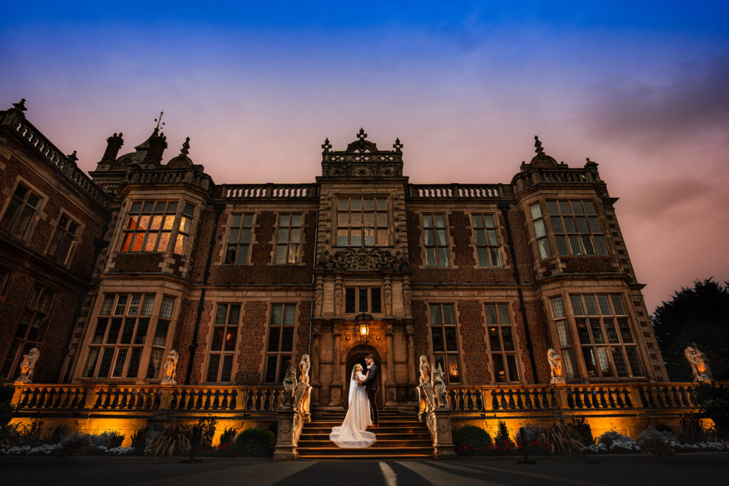 Bride and groom outside a floodlit country house wedding venue at twilight