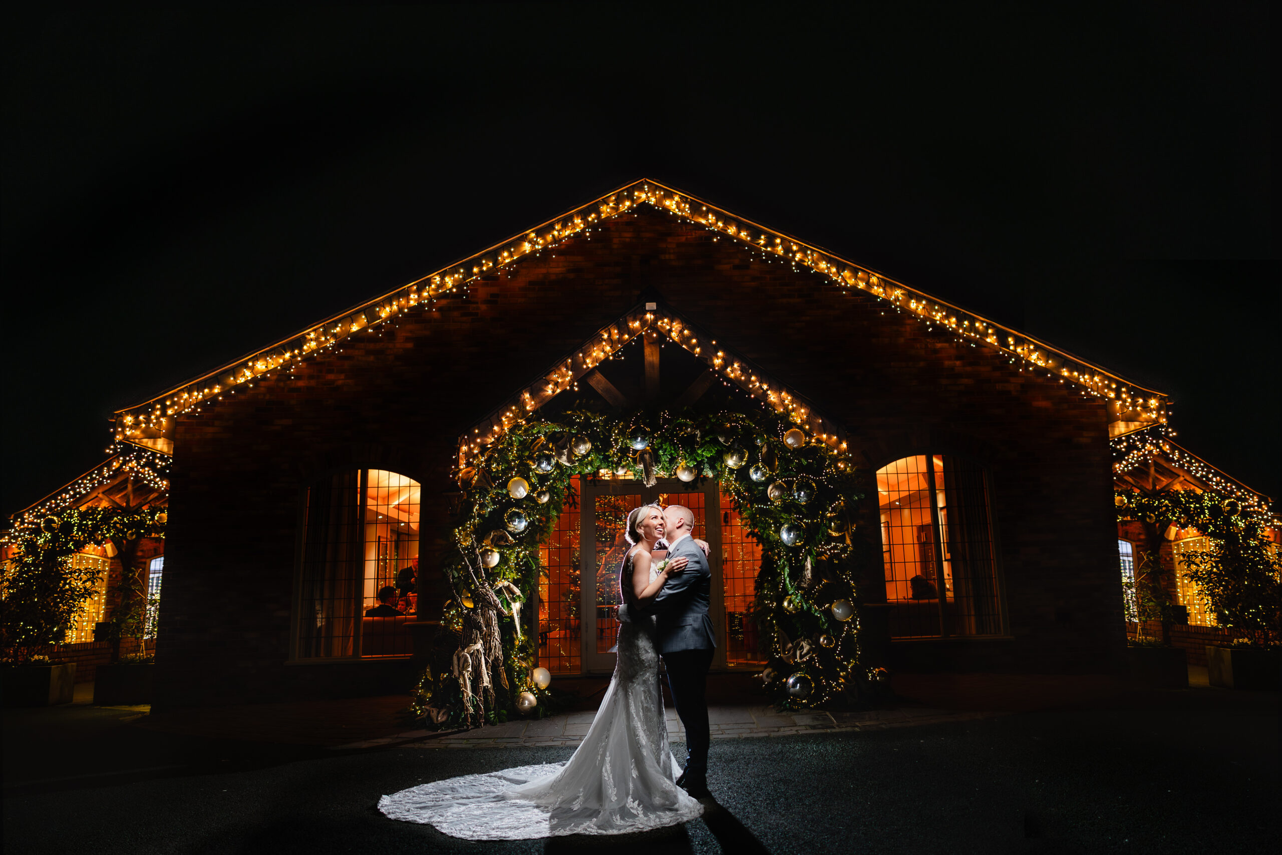 Bride and groom kissing outside the Ceremony Hall at Colshaw Hall, the whole building lit with warm fairy lights on a winter night, Cheshire wedding photographer