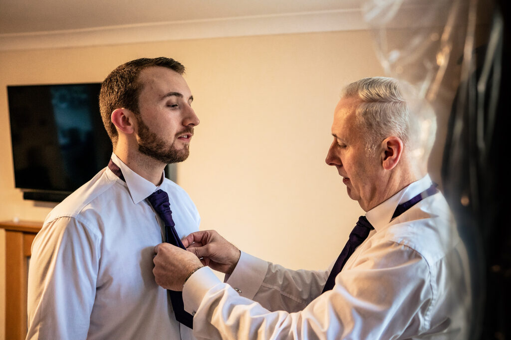 Groom's dad straightening his purple tie on the wedding morning, Merrydale Manor wedding photographer Cheshire