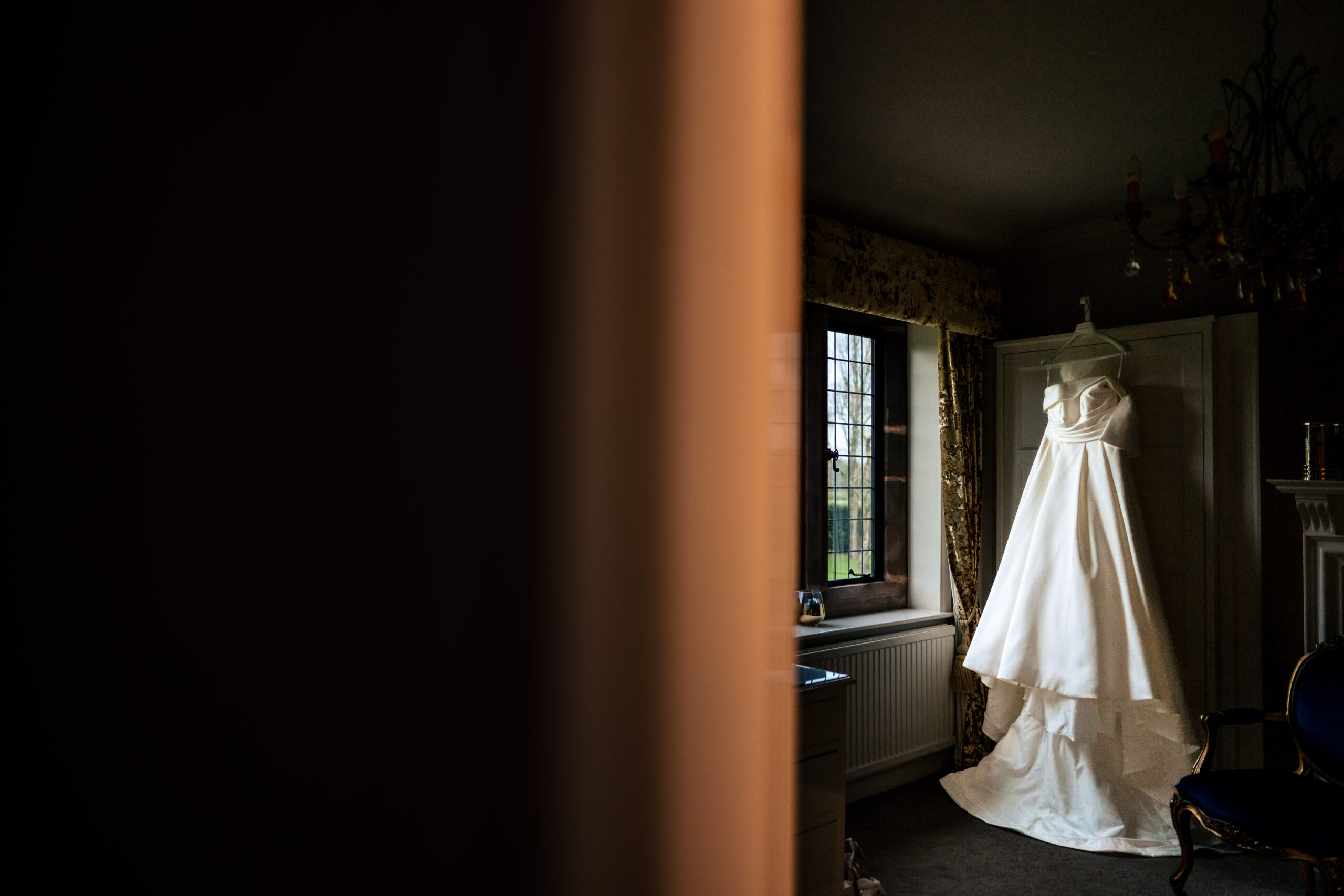 Georgia’s wedding dress hanging in the window light at Colshaw Hall, ready for the morning ahead