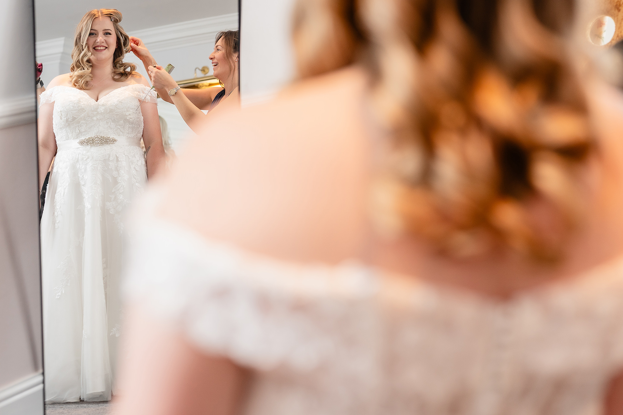 Close up of the bride’s off the shoulder lace wedding dress being fastened up her back at Crewe Hall, Cheshire wedding photographer