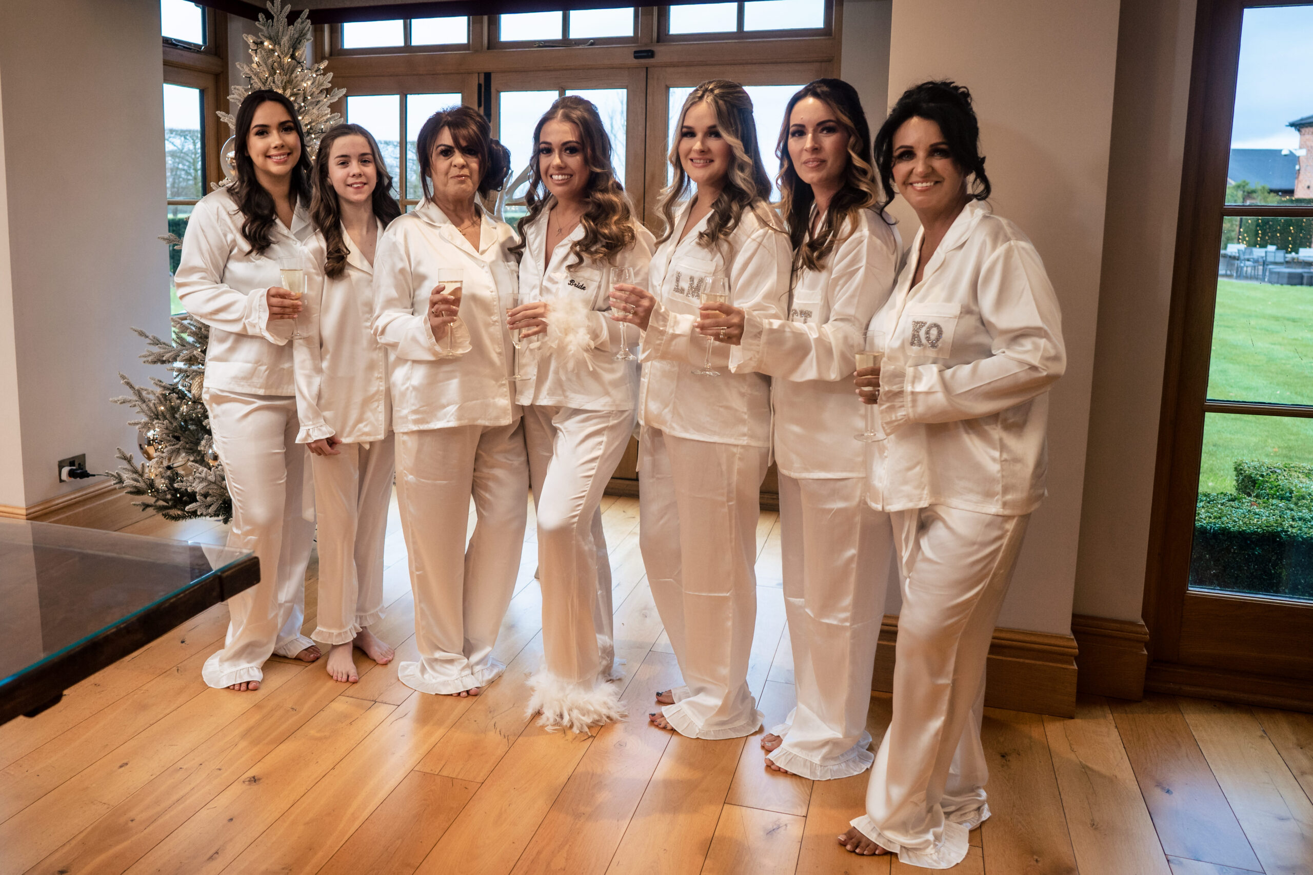 Abbie and her bridal party in matching white satin pyjamas holding glasses of fizz on the wedding morning at Merrydale Manor
