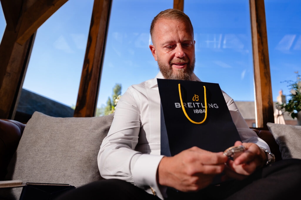 Glynn looking down at his new watch with the Breitling bag on his lap, Swancar Farm Country House, Nottingham wedding photographer