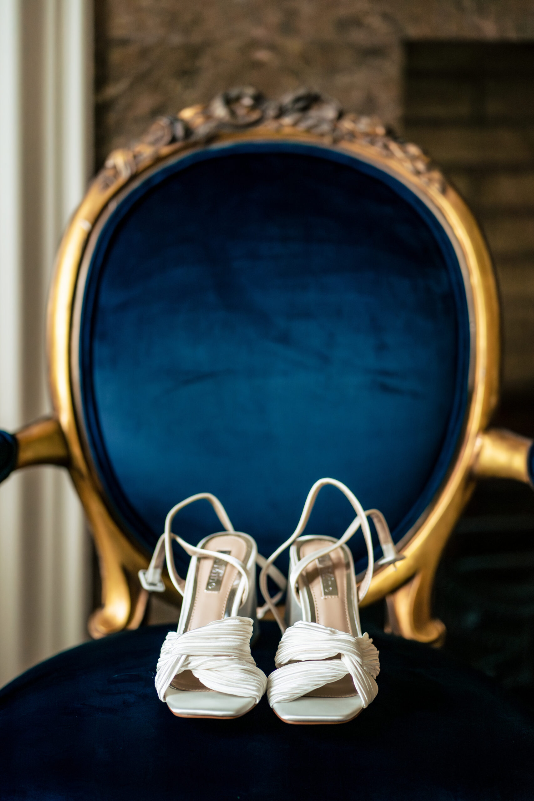 Bridal shoes resting on a blue velvet chair during getting ready at Colshaw Hall