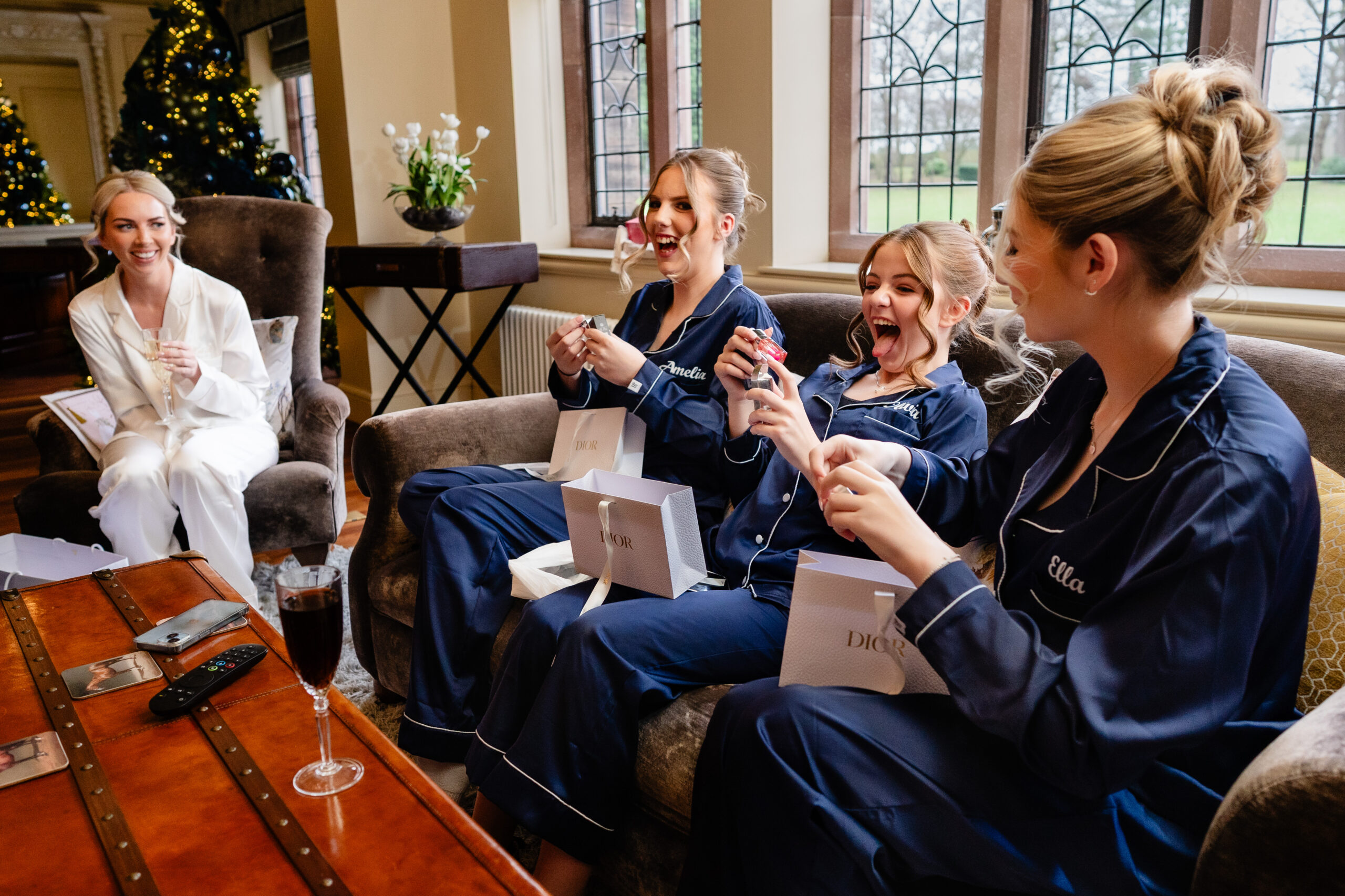 Bridesmaids in navy personalised pyjamas opening gifts beside the Christmas tree during wedding morning prep at Colshaw Hall