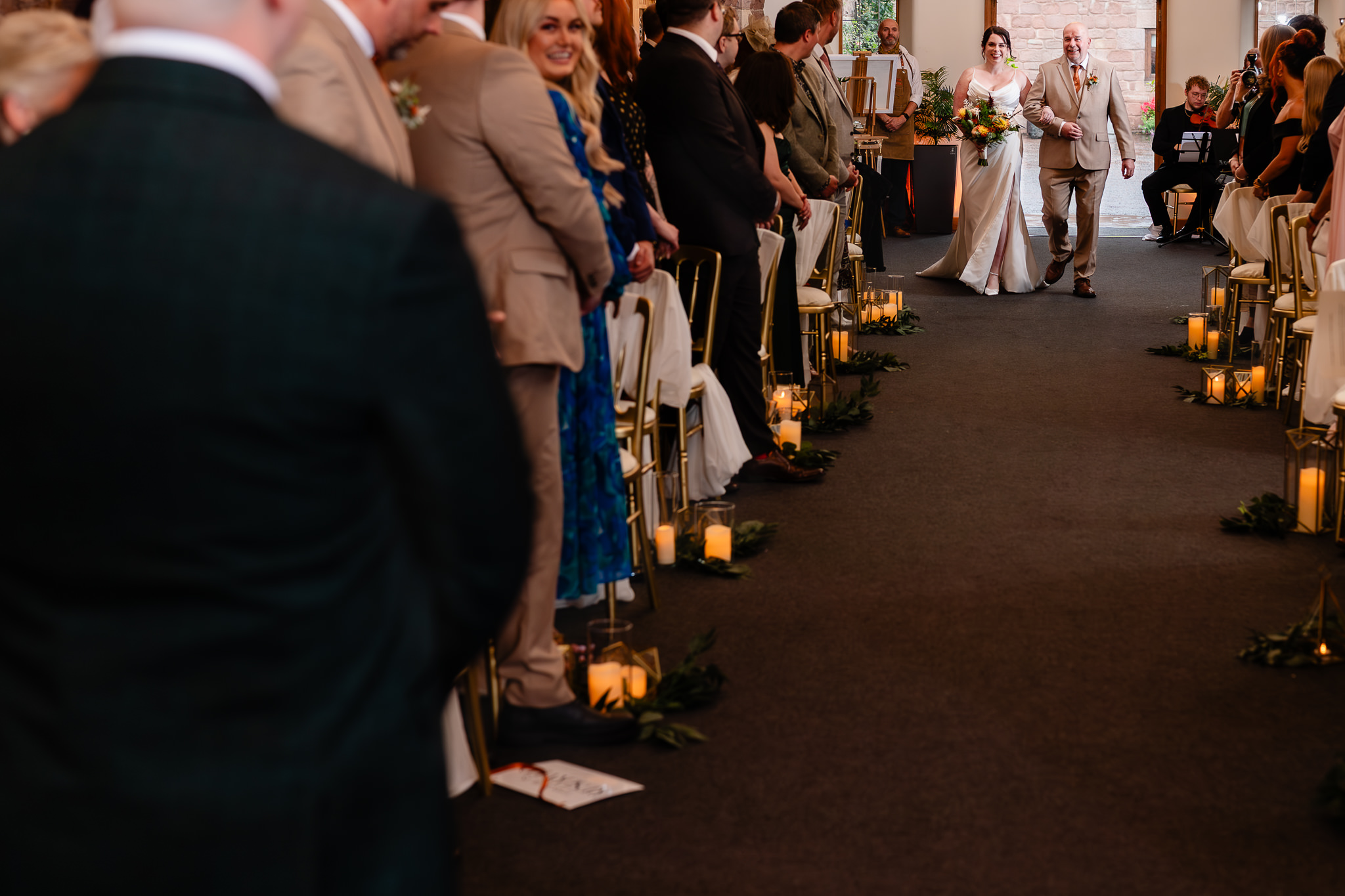 Guests standing as the bride comes down the candlelit aisle at Heaton House Farm, Cheshire wedding photographer