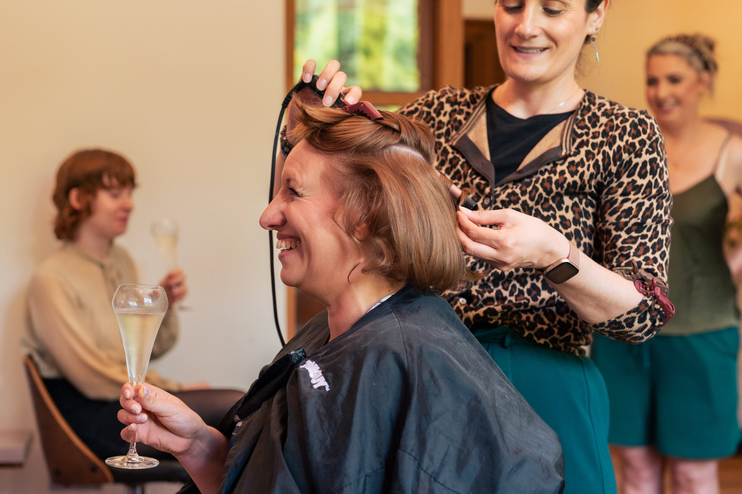 Bride having her hair styled on the morning of her Salt House wedding while a bridesmaid looks on with a glass of fizz