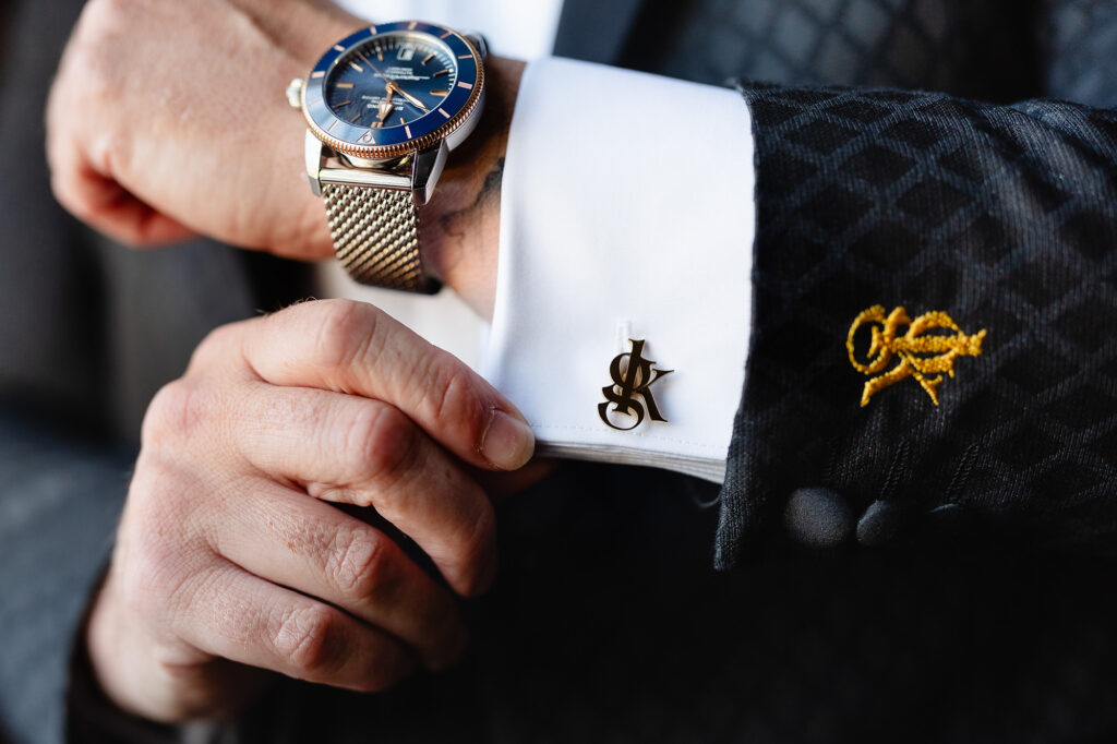 Close up of Glynn's watch, GK monogram cufflink and gold embroidered crest on his black dinner jacket, Swancar Farm wedding photographer