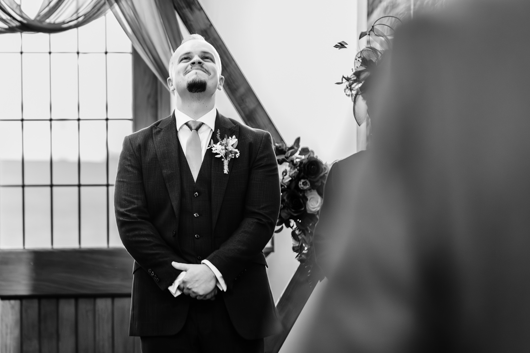 Black and white photo of the groom looking up and holding back tears as his bride arrives, Heaton House Farm wedding ceremony