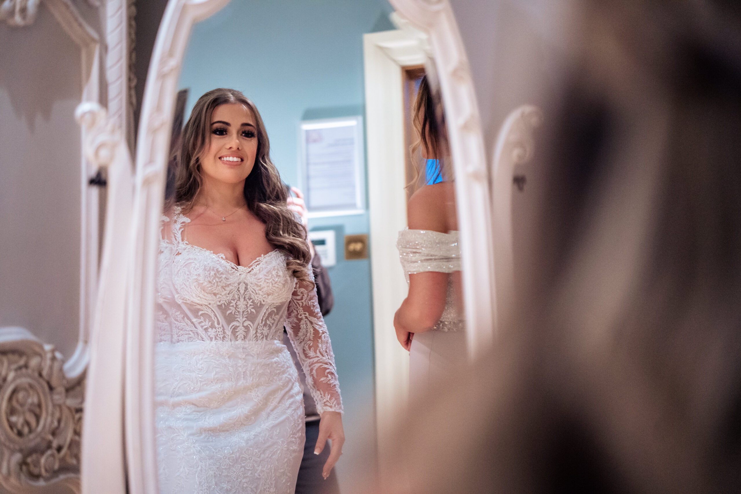 Abbie smiling at her reflection in a white framed mirror with her wedding dress on, Merrydale Manor