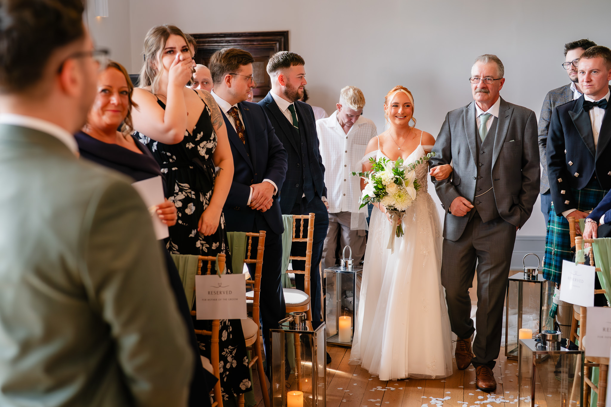Kim walking down the aisle on her dad’s arm, guests smiling either side at Salt House