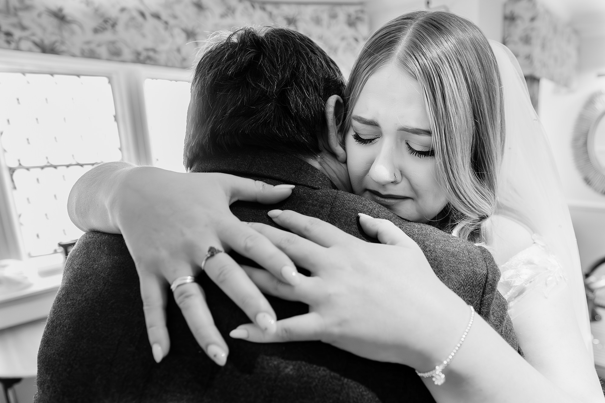 Black and white shot of the bride wiping away tears in her dad’s arms before walking down the aisle, Crewe Hall wedding photographer