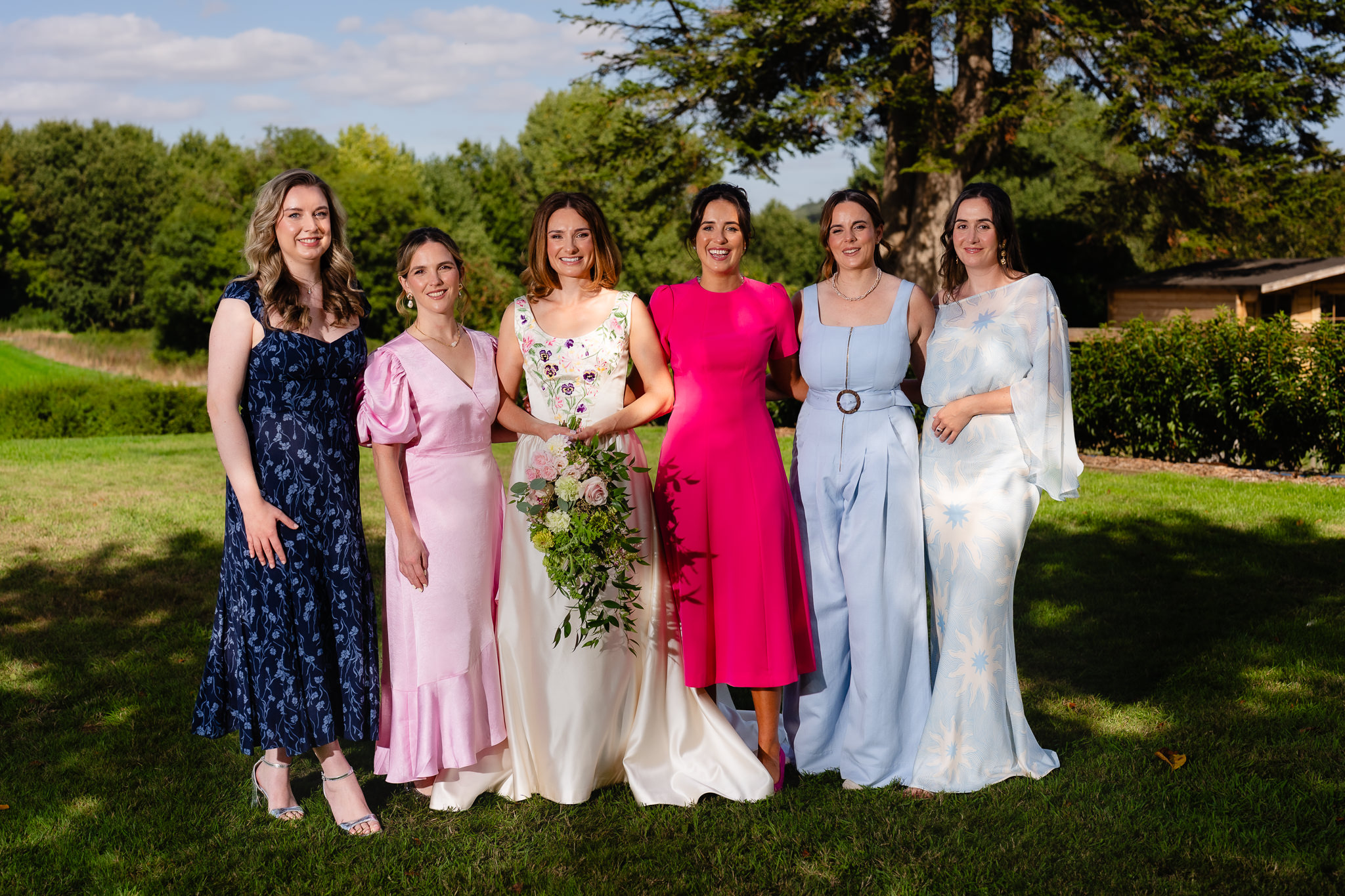 Bridesmaids in mismatched dresses laughing together in the garden before the ceremony, Dorset wedding photographer