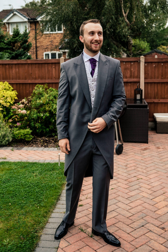 Full length portrait of the groom in a grey morning suit and purple tie in the garden, Cheshire wedding photographer