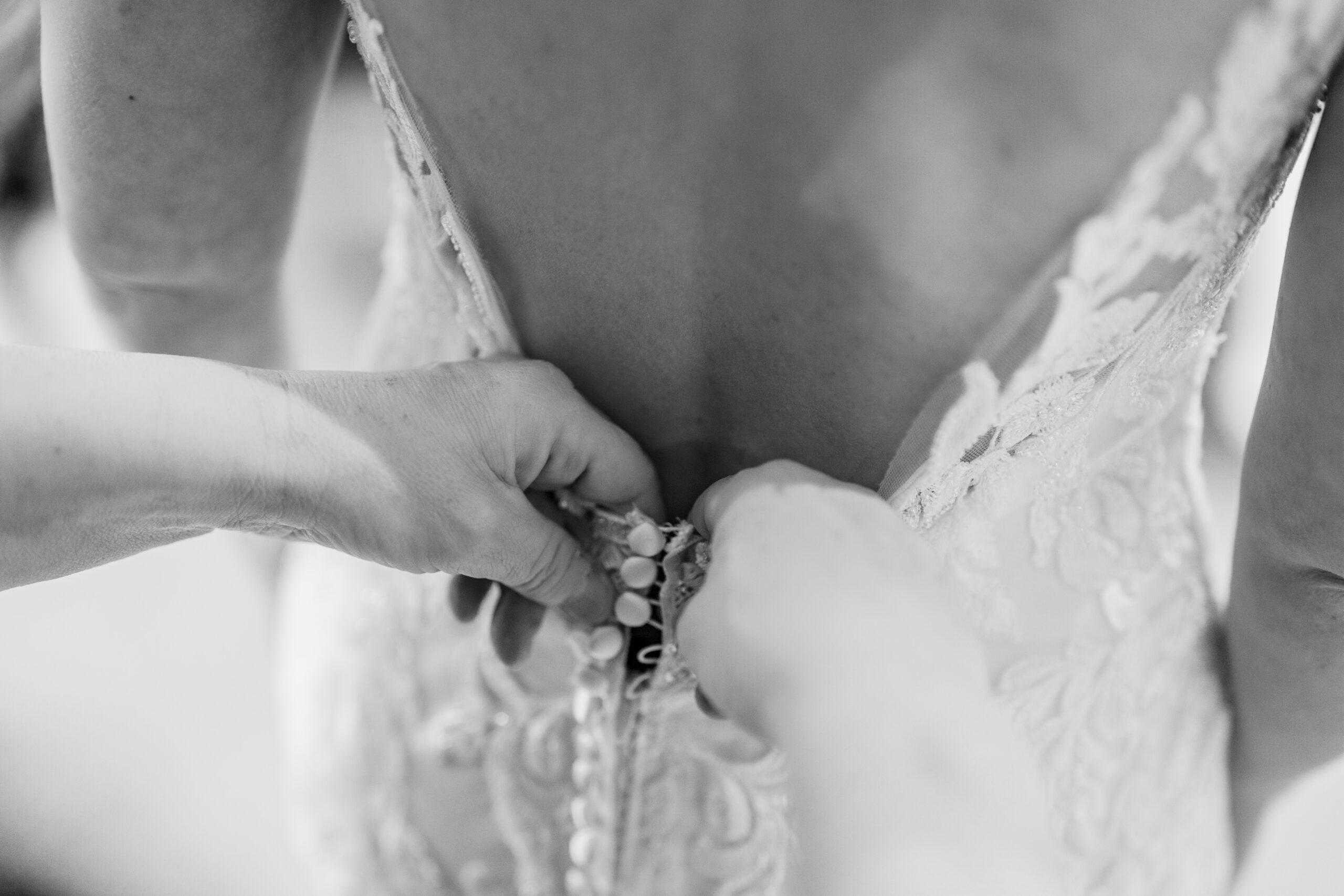 Black and white close up of the lace wedding dress being buttoned up at the back, Cheshire wedding photographer