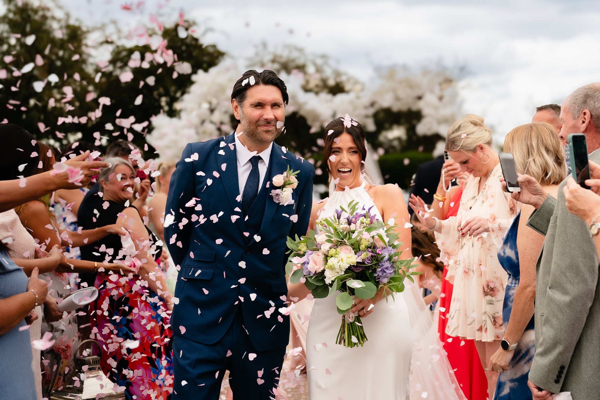 Bride and groom laughing as guests throw pink confetti at Salt House, Staffordshire wedding photographer