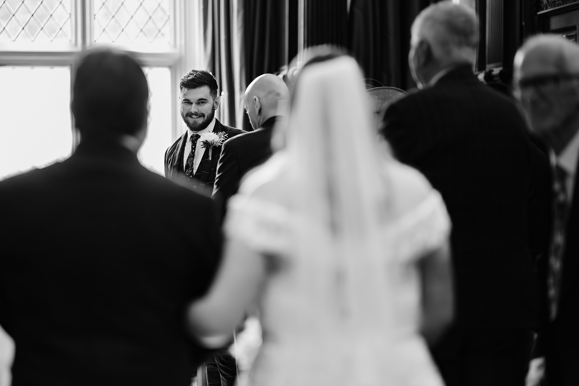 Black and white shot of the groom and guests turning to watch the bride arrive at the top of the aisle, Crewe Hall wedding photographer