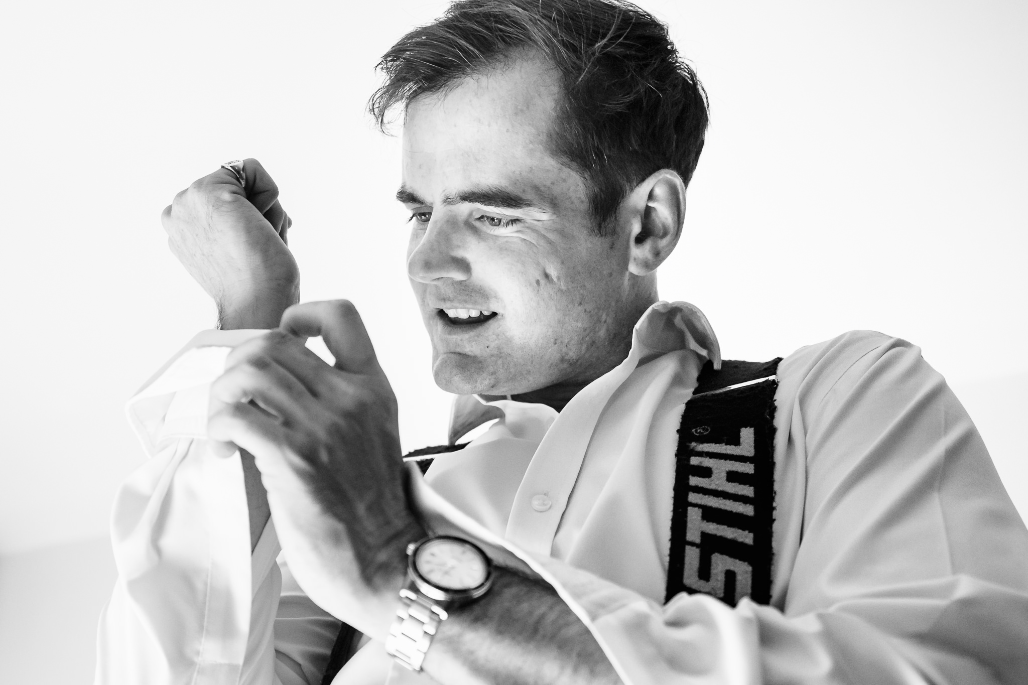 Black and white portrait of the groom fastening his shirt on the wedding morning