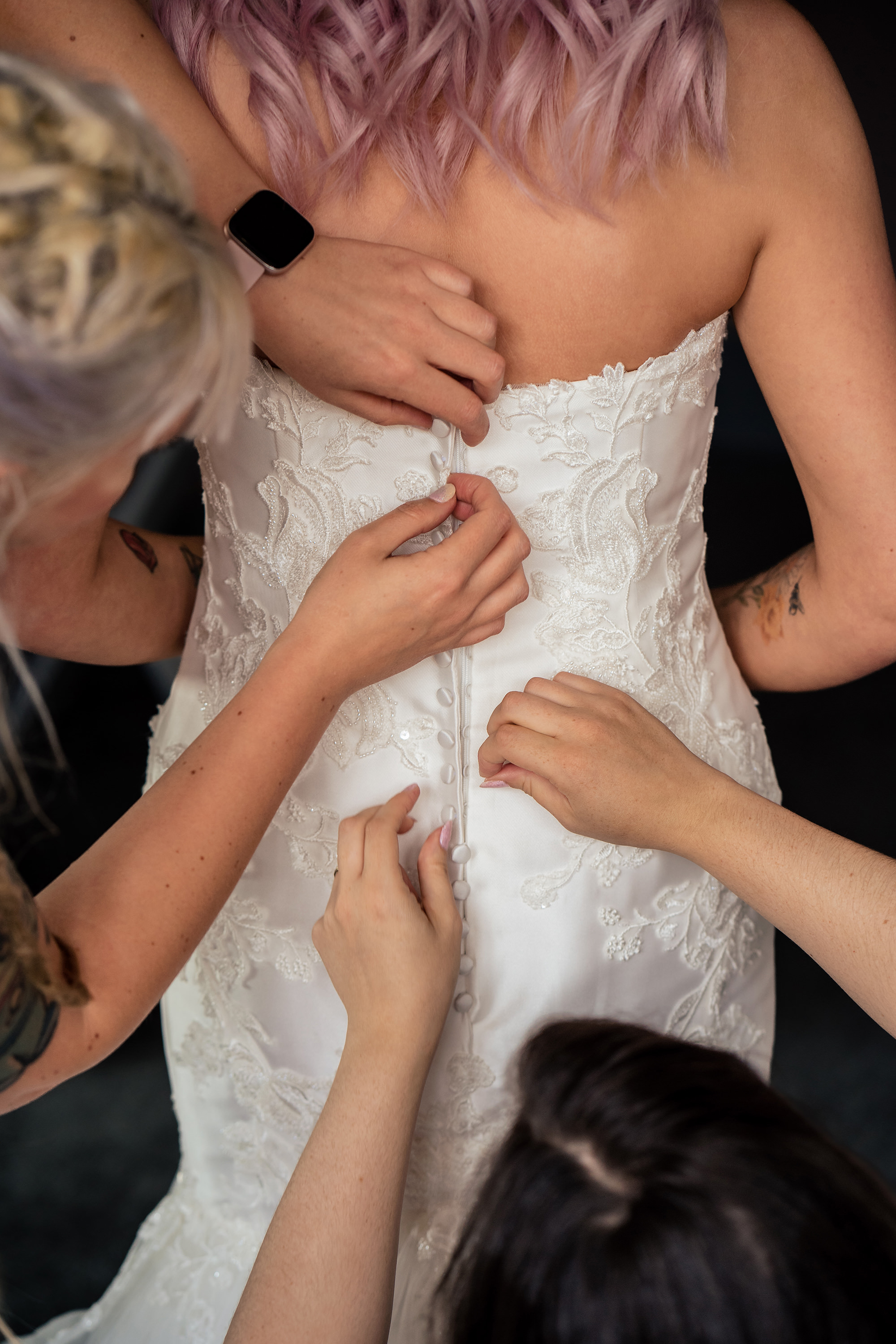 Bridesmaids buttoning the bride into her lace wedding dress, Standon Hall wedding photographer