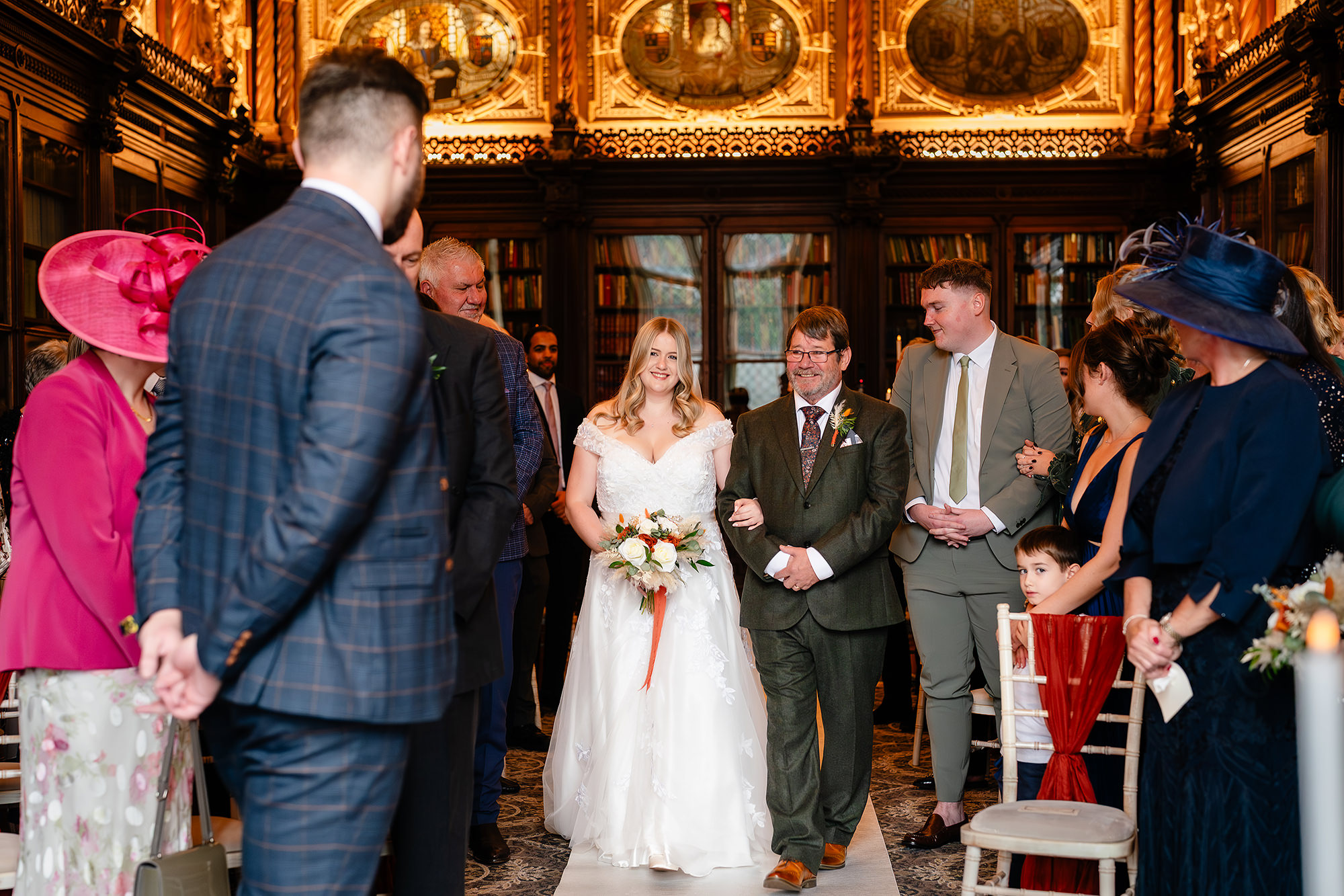 Guests seated in Crewe Hall’s ornate ceremony room as the bride walks down the aisle, Cheshire wedding photographer