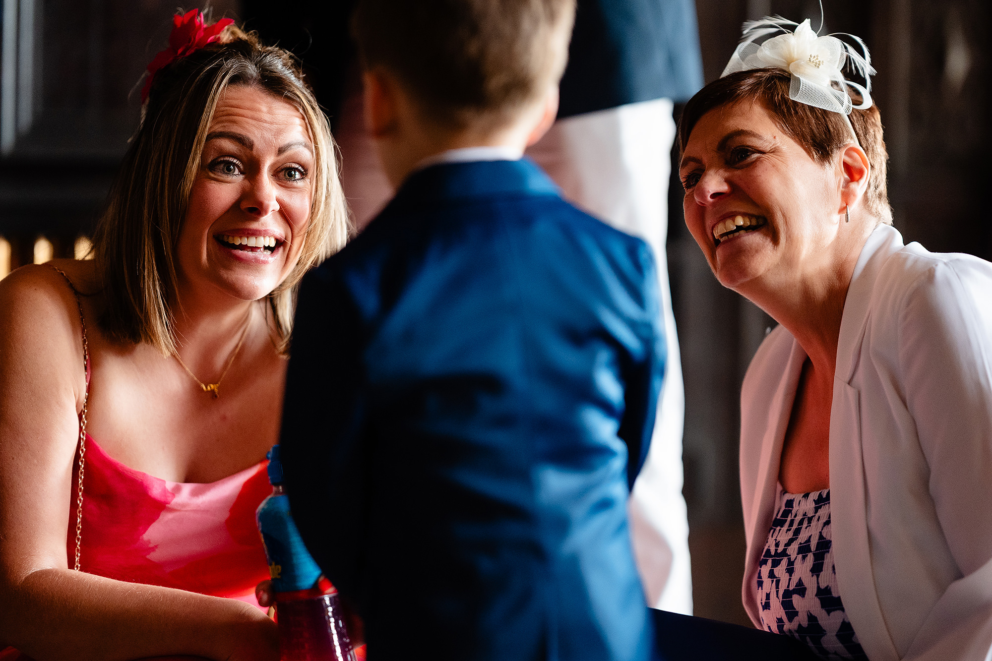 Two women laughing with a small boy in a navy suit as everyone gets ready at Crewe Hall