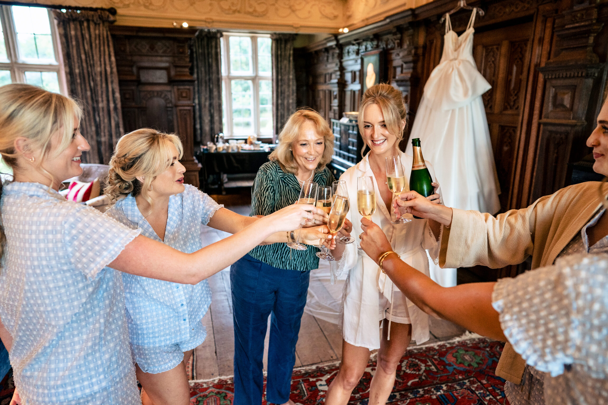 Bride and her bridesmaids clinking champagne glasses in the panelled bridal suite, Dorfold Hall wedding photographer