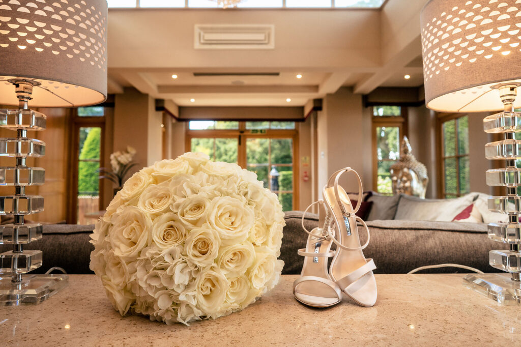 White rose bridal bouquet and strappy heels on a table in the bridal suite at Merrydale Manor