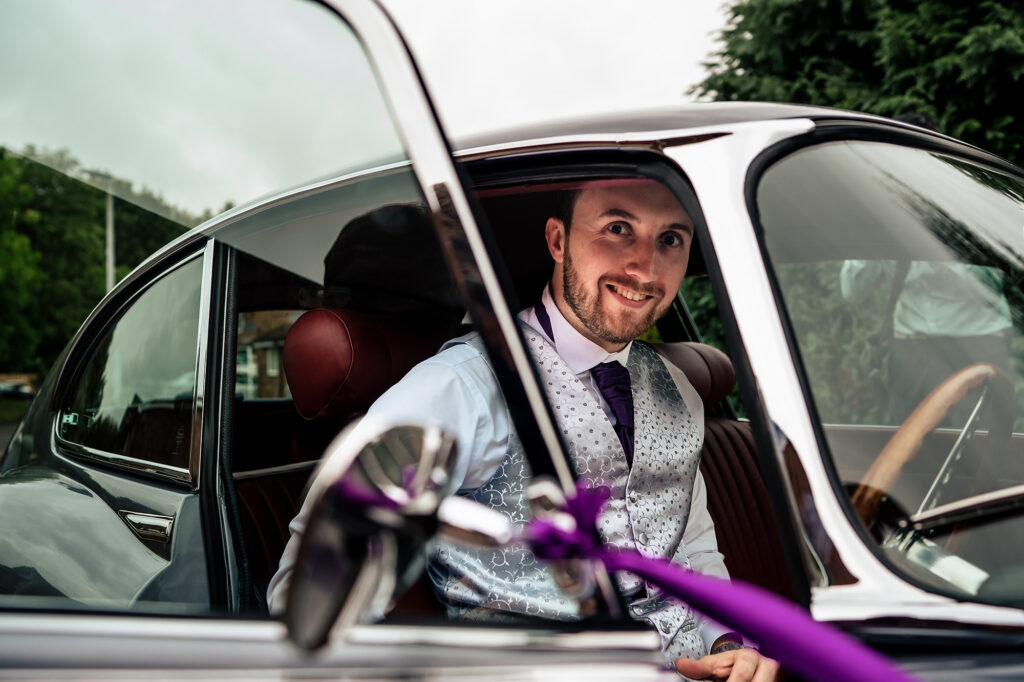 Groom grinning from the driver's seat of the restored E-type Jaguar, Merrydale Manor wedding photographer