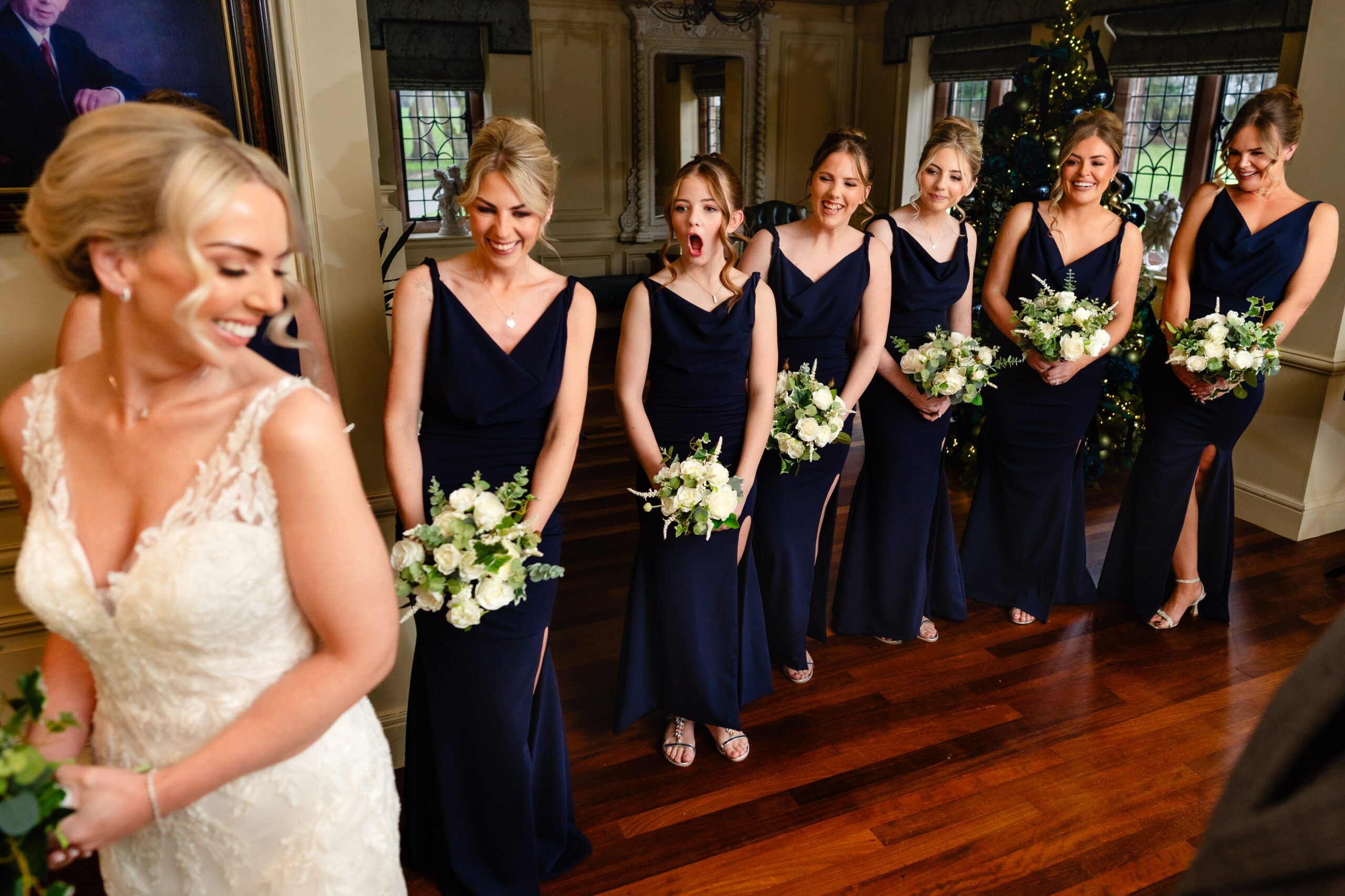 Bride laughing with her seven bridesmaids in navy dresses holding white winter bouquets, Colshaw Hall wedding