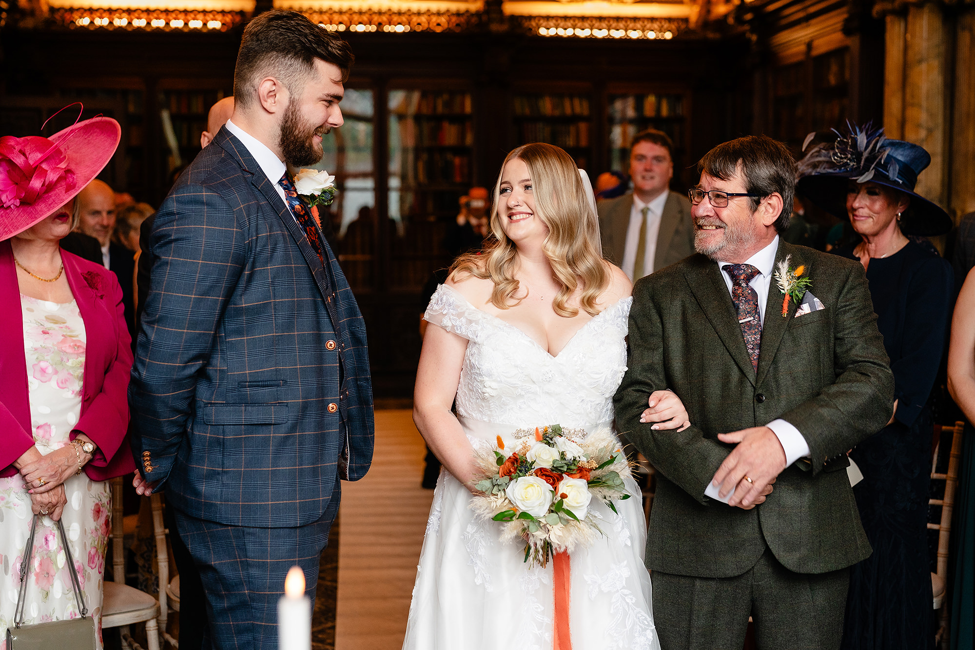 Annie and Tom smiling at each other during their ceremony, surrounded by seated guests, Crewe Hall wedding photographer
