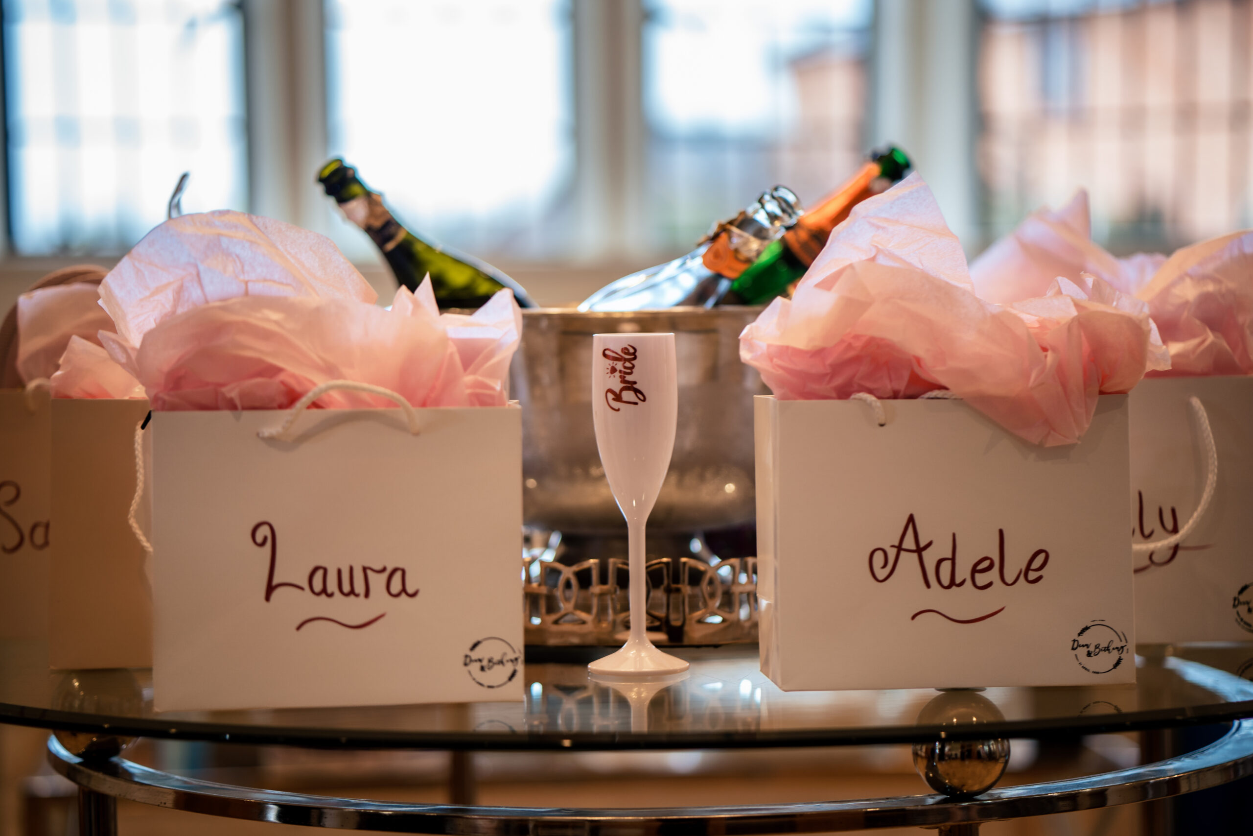 Gift bags with handwritten names and a bride flute beside an ice bucket of fizz in the bridal suite