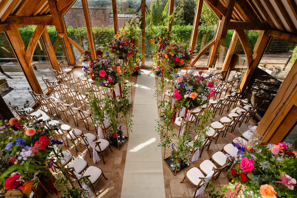 The glass barn set for the ceremony, aisle lined with hot pink, orange, purple and cobalt florals, Swancar Farm wedding photographer