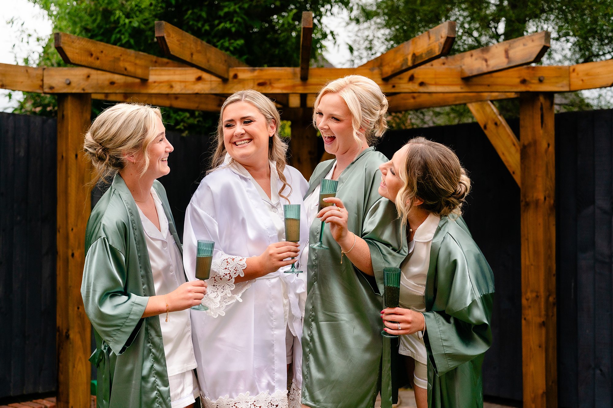 The bridesmaids toasting with drinks in sage green robes on the morning of the wedding