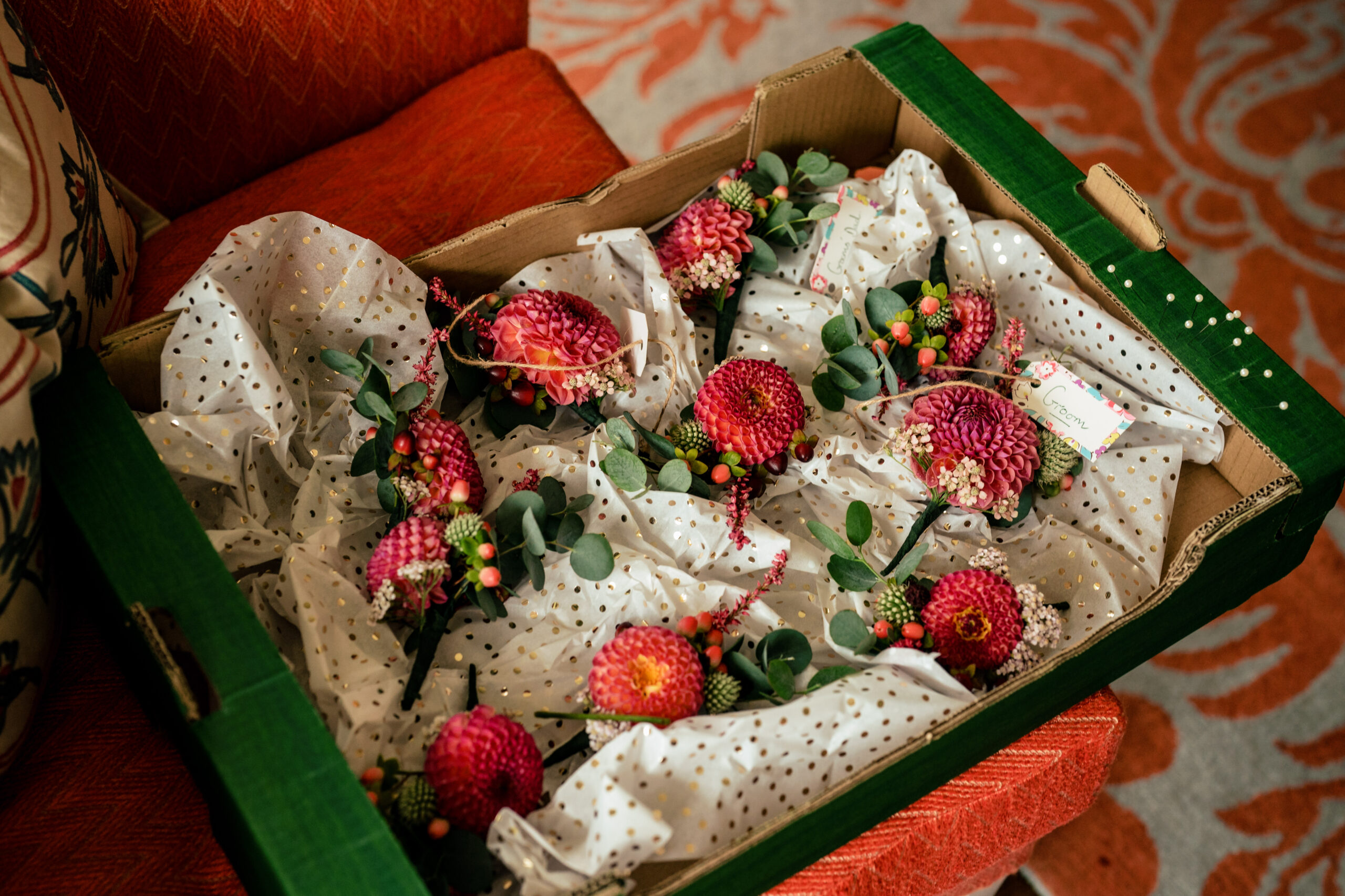 Boxed buttonholes of deep red dahlias and eucalyptus waiting for the groomsmen at Dorfold Hall