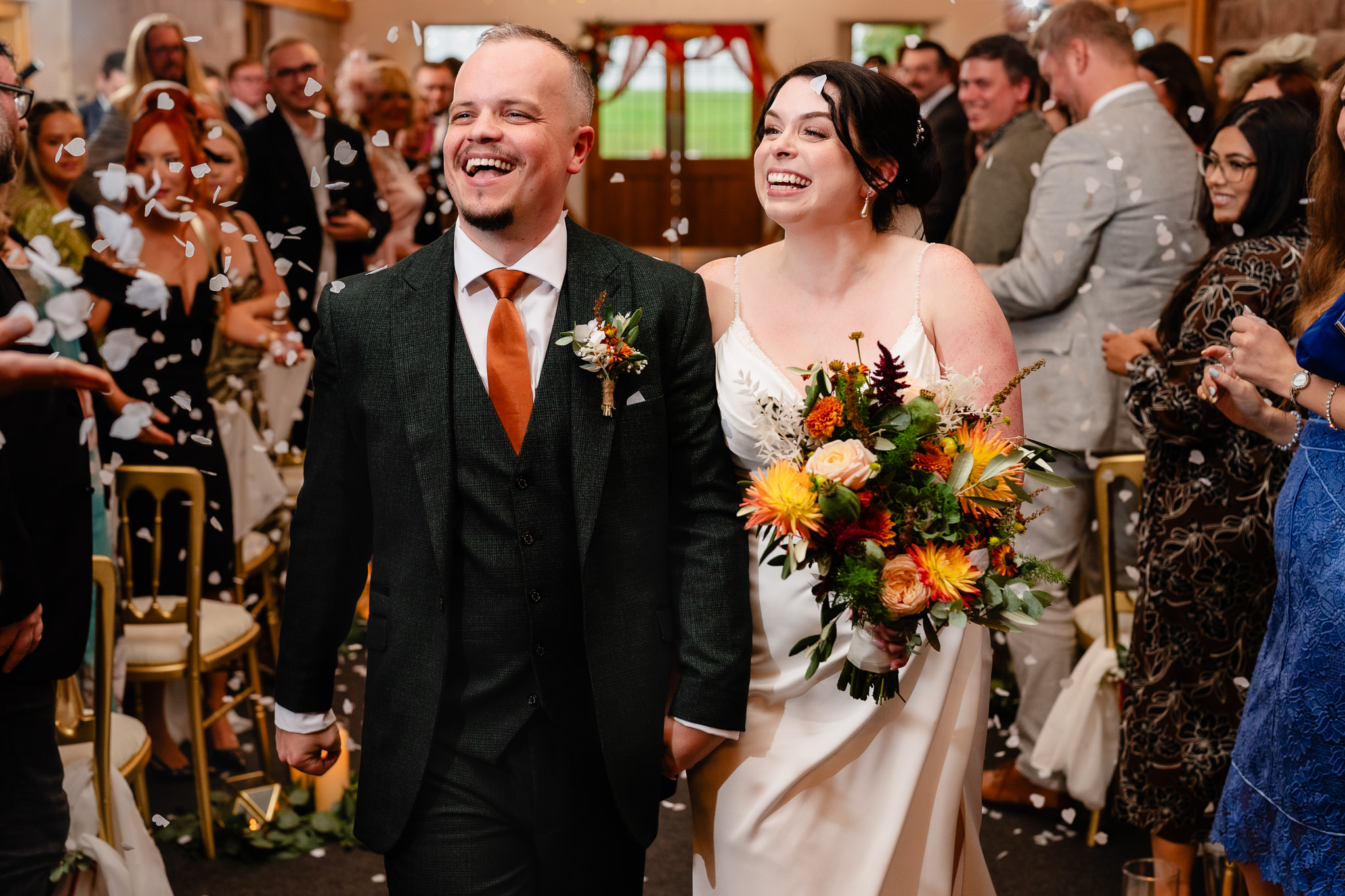 Close up of the bride and groom laughing as petals fall around them, autumn bouquet in her hand, Heaton House Farm wedding