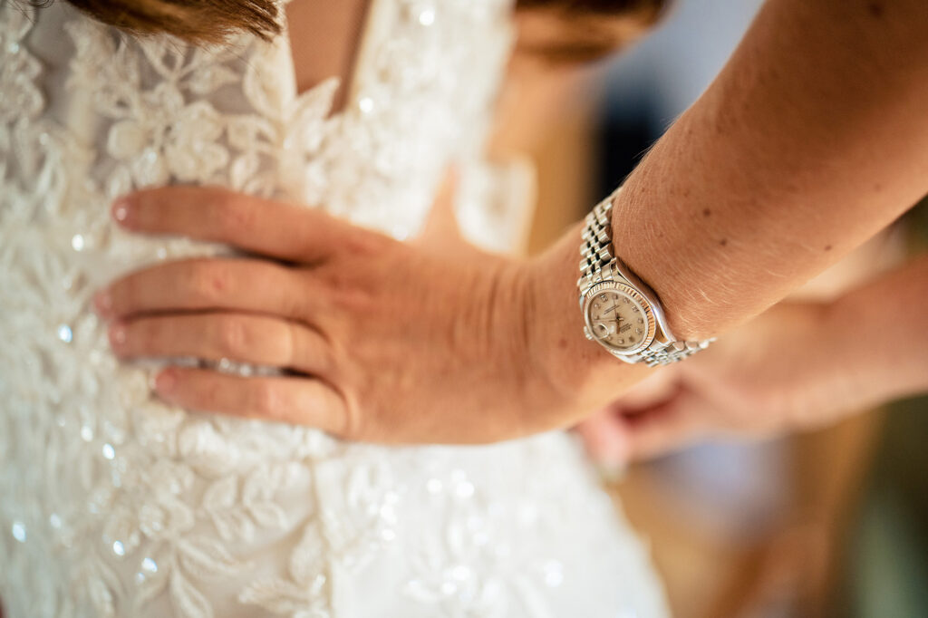 A hand with a silver watch fastening the back of Gemma’s lace wedding dress