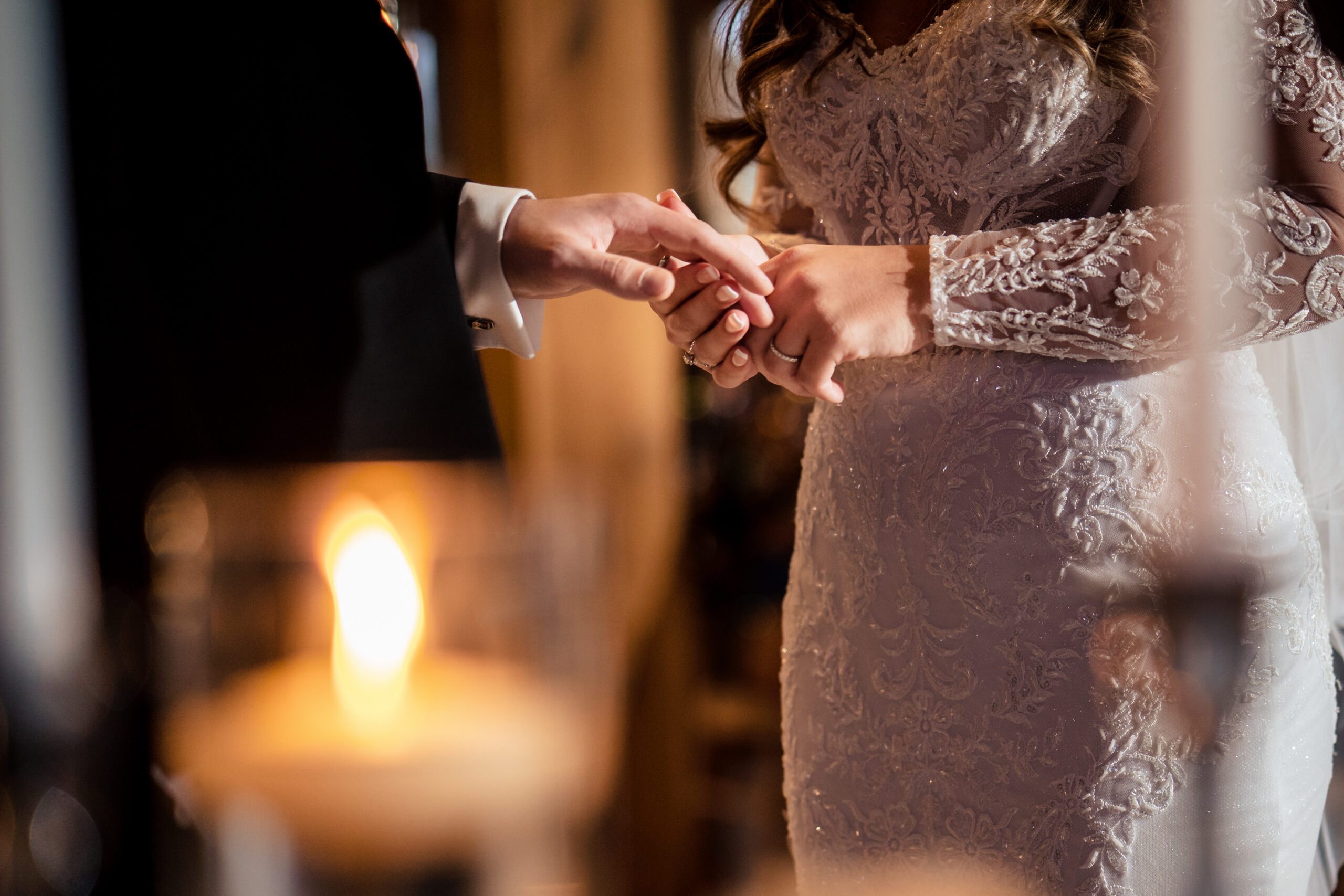 Close up of the rings being exchanged behind a glowing candle during the ceremony at Merrydale Manor