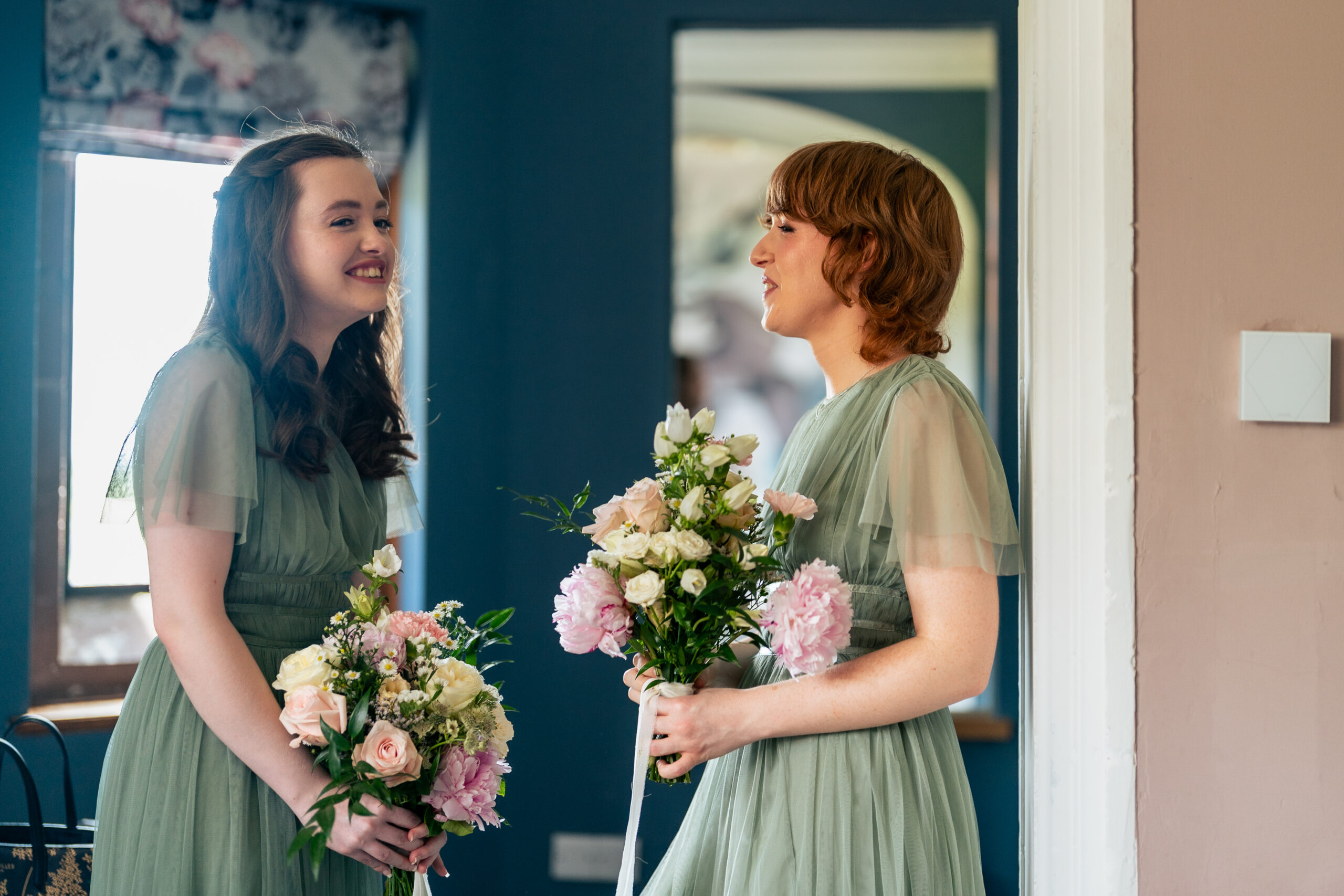 Two bridesmaids in sage green dresses hugging in a doorway at Salt House moments before the ceremony