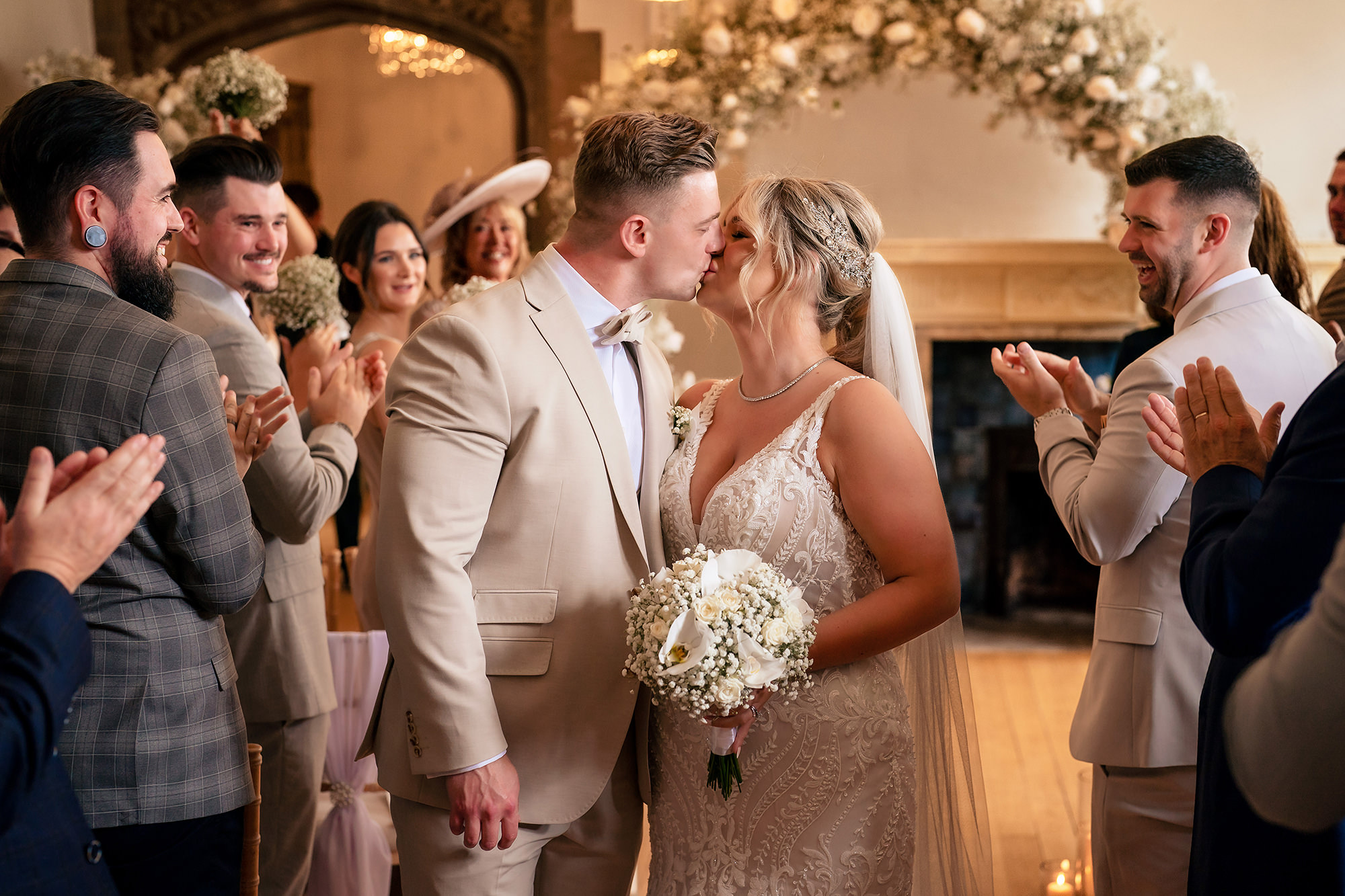 Jess and Cy’s first kiss as a married couple under a floral arch at Salt House, guests applauding
