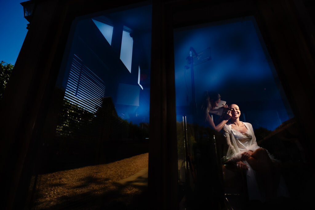 Kim in her robe by the window of the stables cottage, deep blue reflections in the glass, Swancar Farm wedding photographer