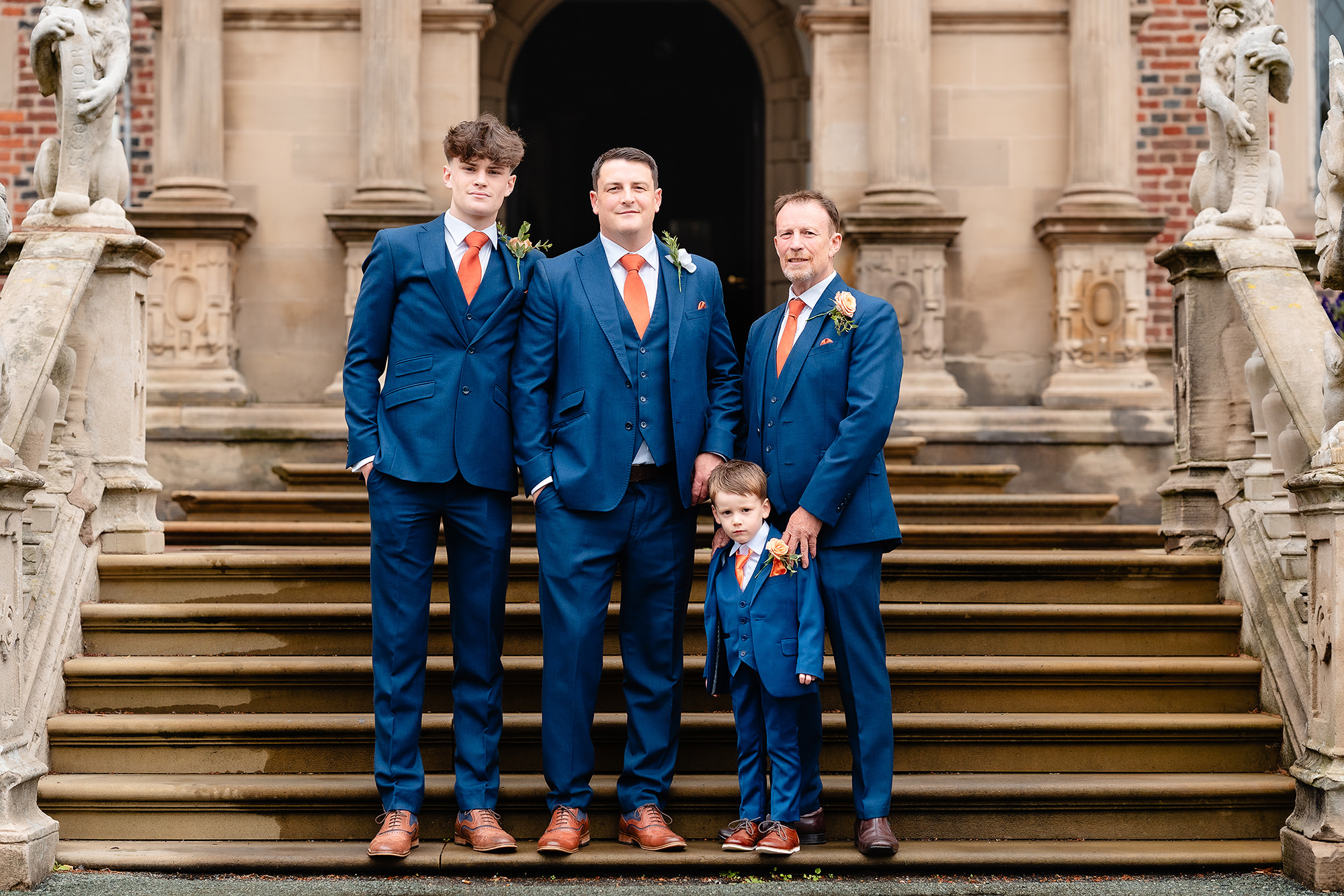 The groom on the steps at Crewe Hall with Zach, Alexander and a guest, all in navy suits with orange ties