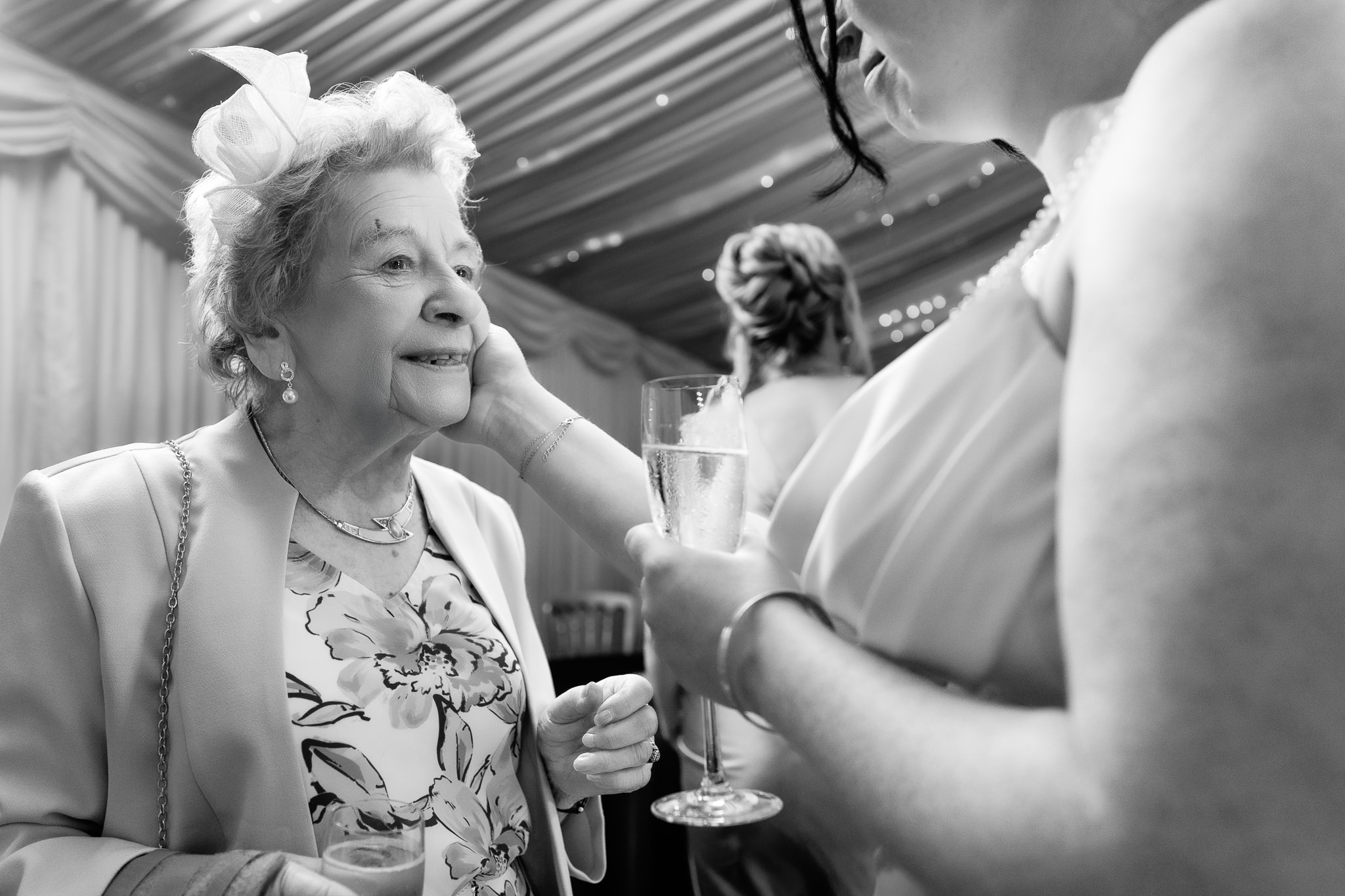 Black and white photo of the bride's grandmother reaching up to touch her cheek during the drinks reception, Heaton House Farm wedding photographer